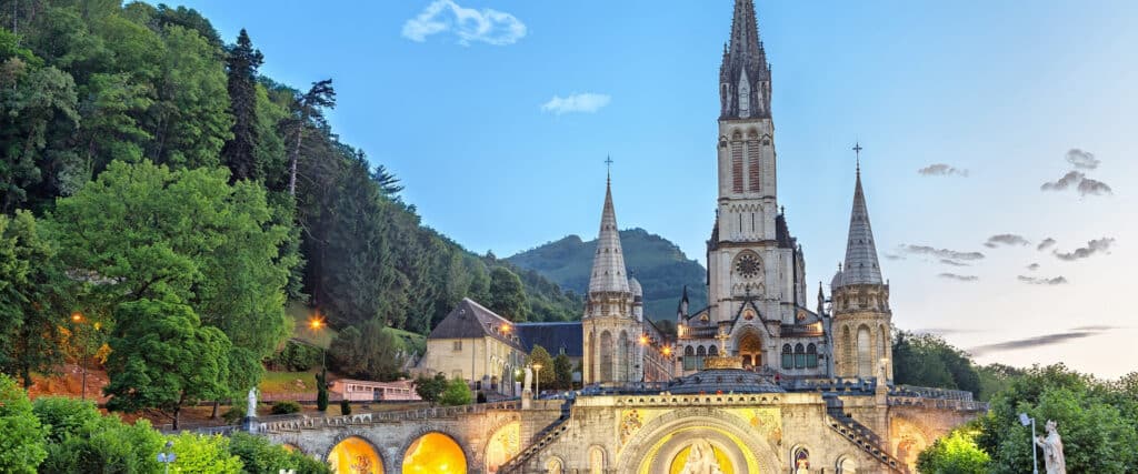 Basilique de Lourdes, France. Ses tours majestueuses se dressent devant des montagnes verdoyantes et un ciel bleu clair.